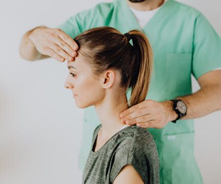 Leistungen Positive bearded doctor in uniform doing rehabilitation neck massage on female patient after injury against gray background